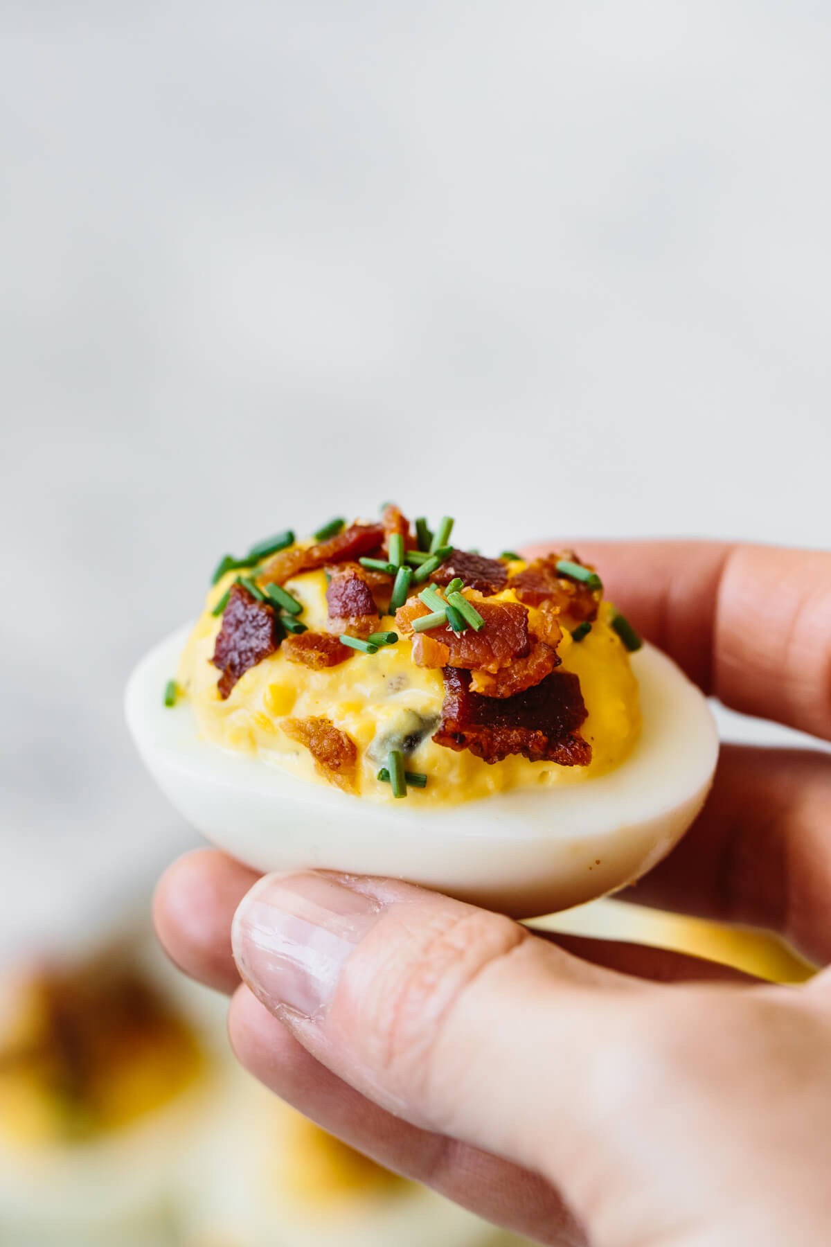 Bacon deviled eggs are the ultimate deviled egg recipe! A deviled egg with bacon held in a hand, about to be eaten.
