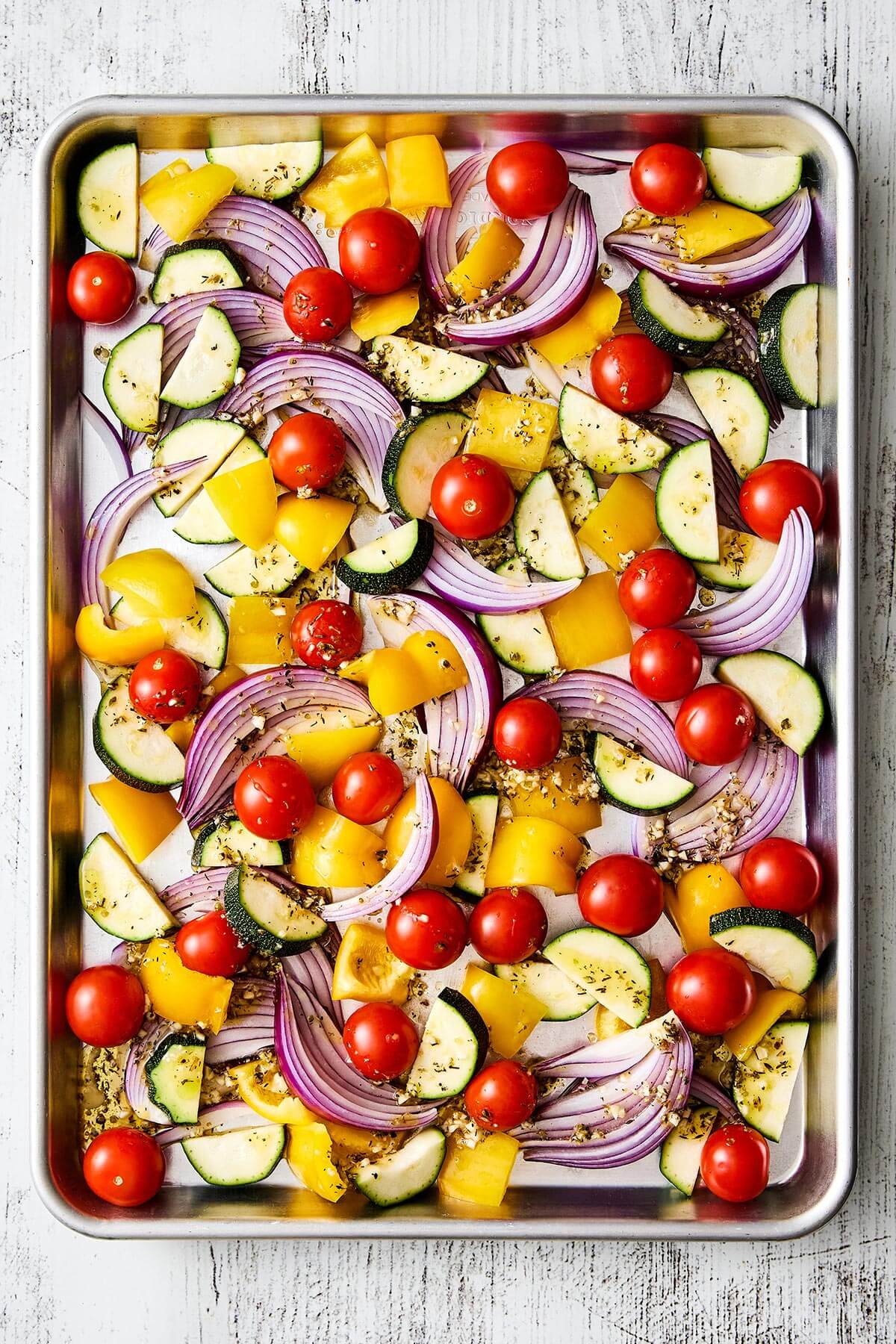 This Greek sheet pan chicken is an easy, all-in-one dinner recipe with juicy chicken thighs nestled around vibrant, Mediterranean vegetables. Seasoned vegetables on a sheet pan.