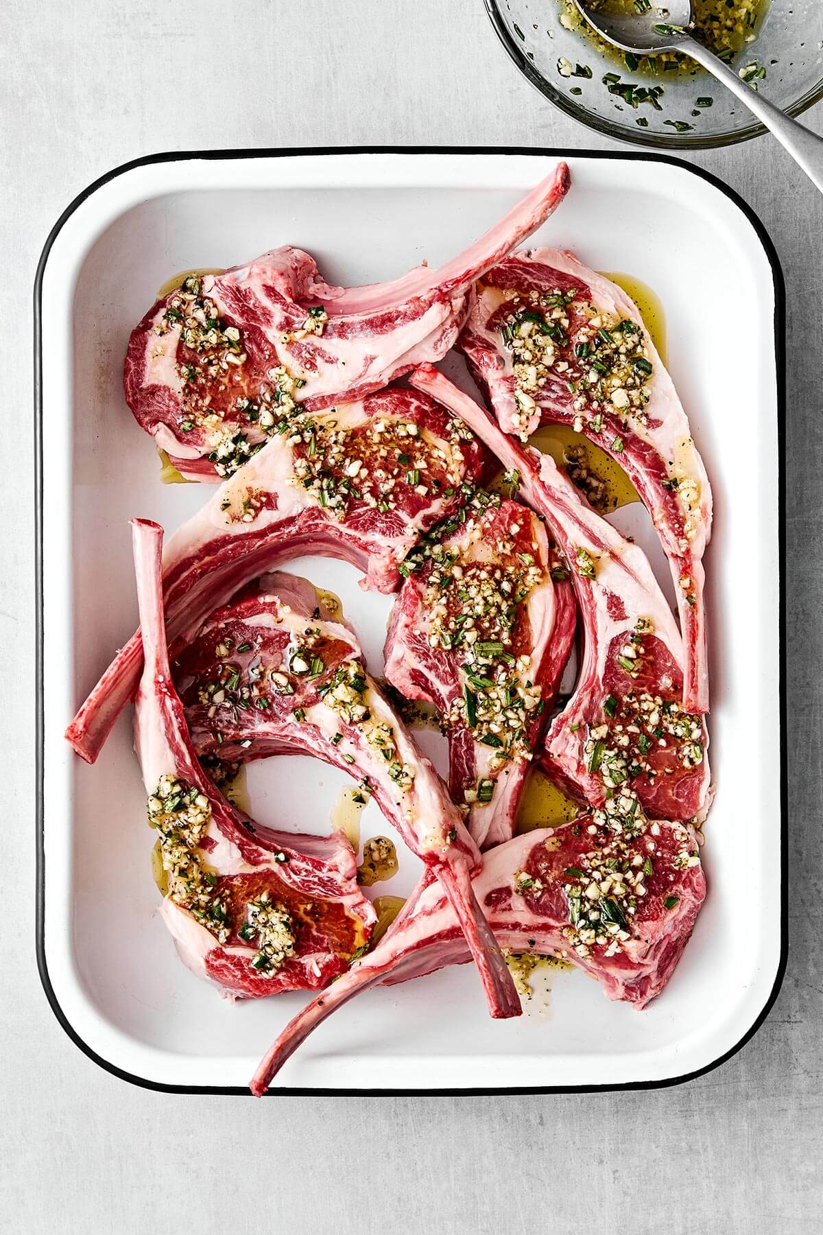 These garlic rosemary lamb chops come off the grill perfectly charred and tender every time—perfect for the holidays and grilling season! A tray of marinated lamb chops filled with garlic and rosemary.
