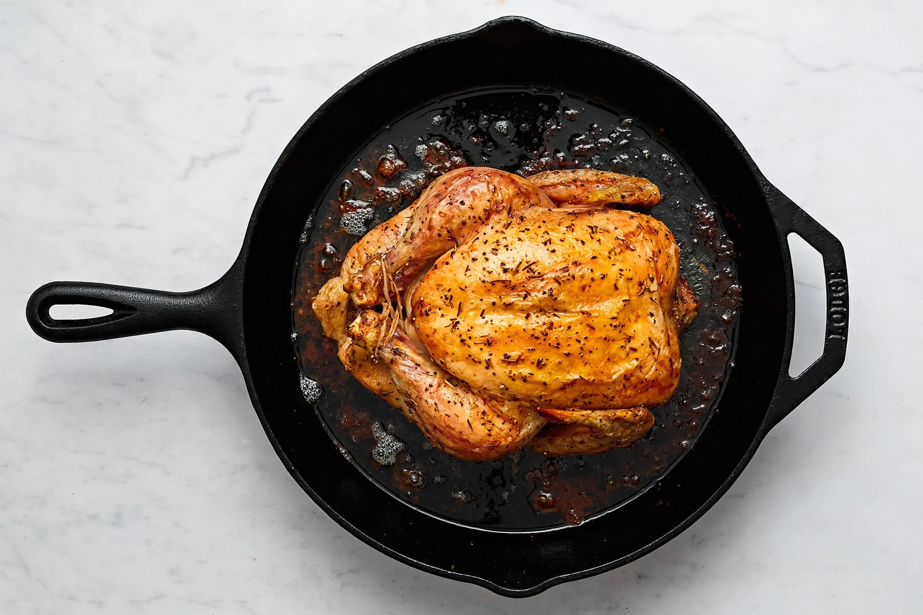 A skillet with a cooked whole roast chicken