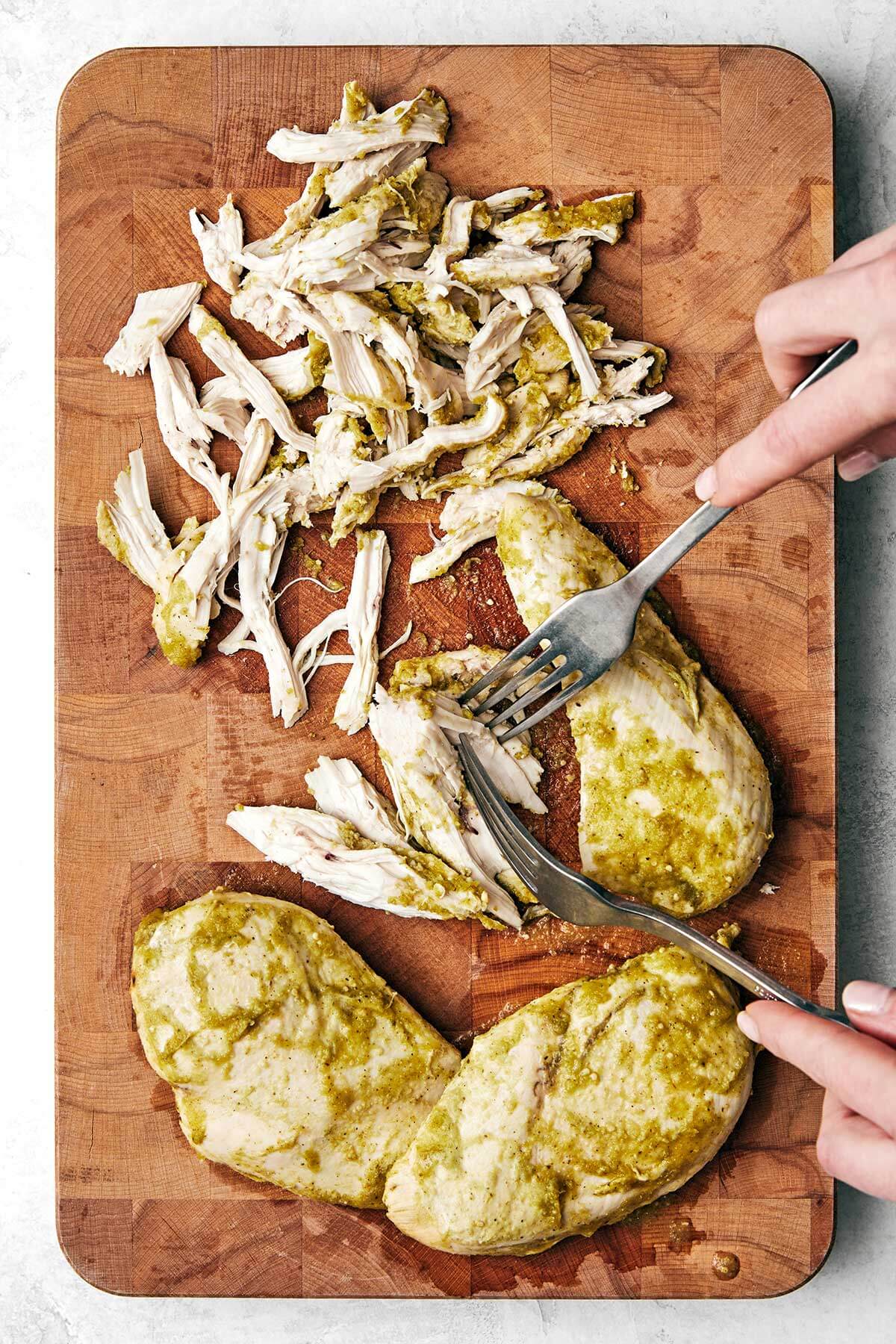 This salsa verde chicken is juicy, tender, and brimming with smoked, tangy, and spicy flavors. Plus, it's made easy right in the slow cooker! Shredding salsa verde chicken on a wooden board.