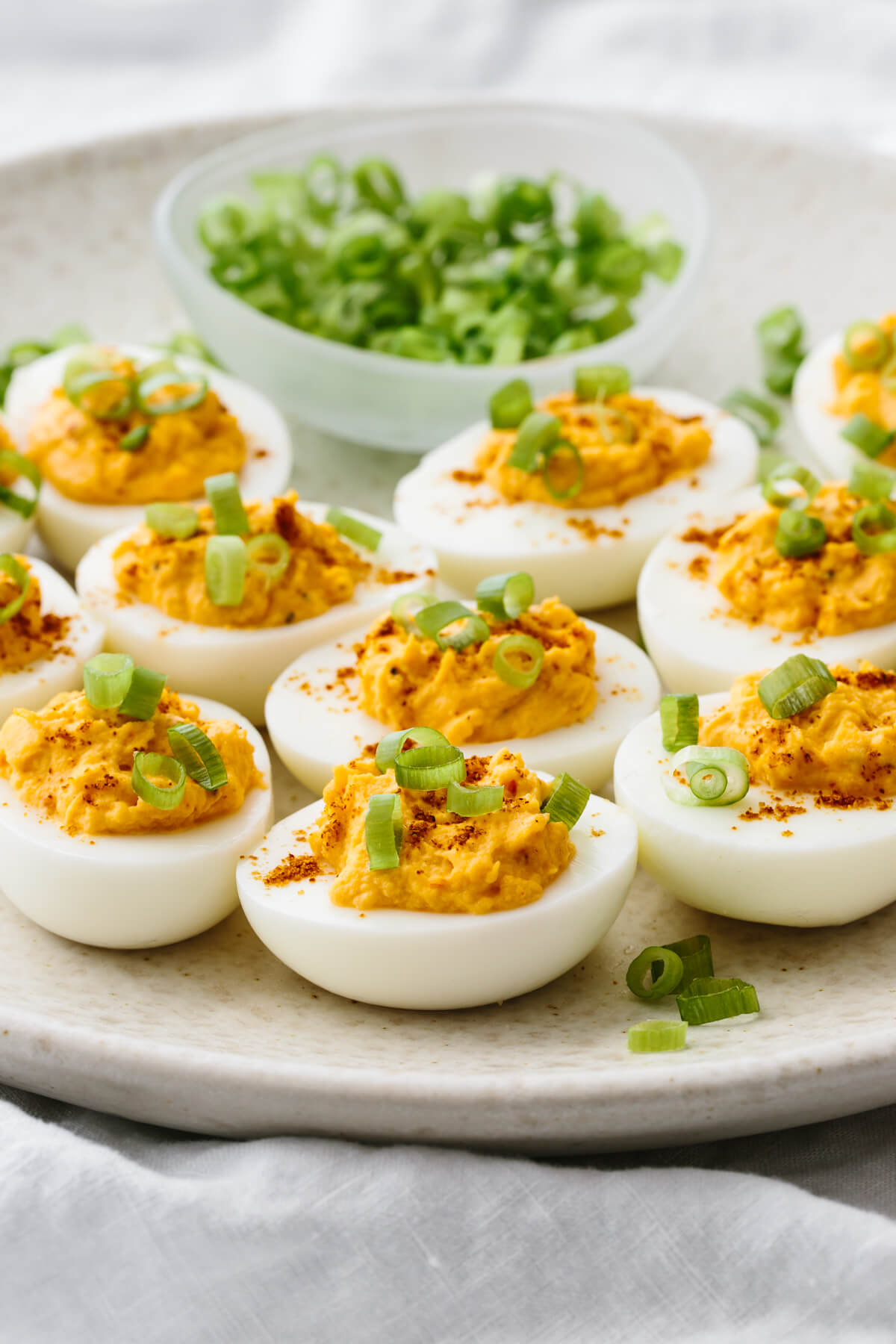 These spicy deviled eggs bring a fiery twist to a classic recipe, with Sriracha, dijon mustard, and cayenne! Spicy deviled eggs next to a bowl of green onions.