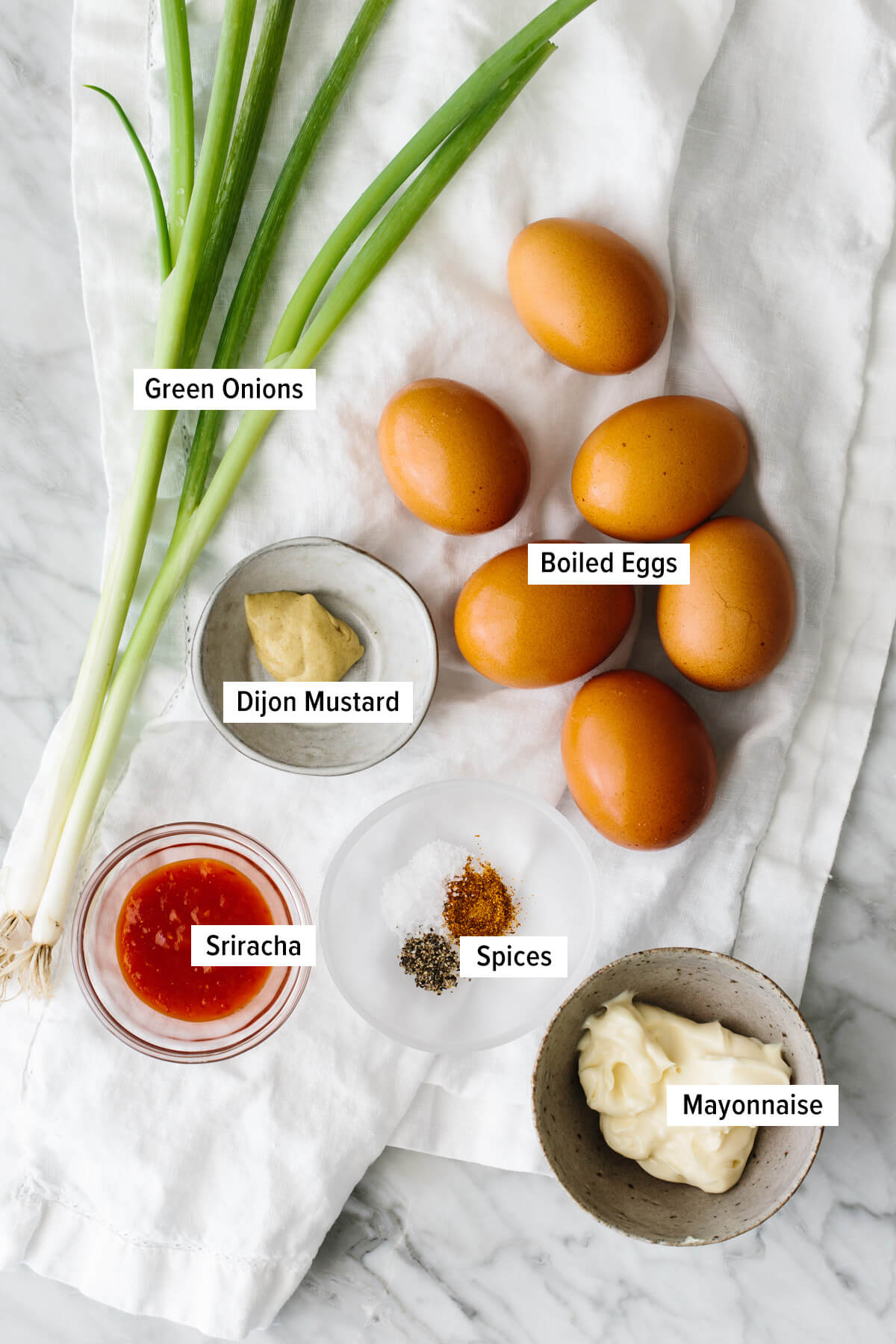 These spicy deviled eggs bring a fiery twist to a classic recipe, with Sriracha, dijon mustard, and cayenne! Ingredients for spicy deviled eggs laid out on a table.