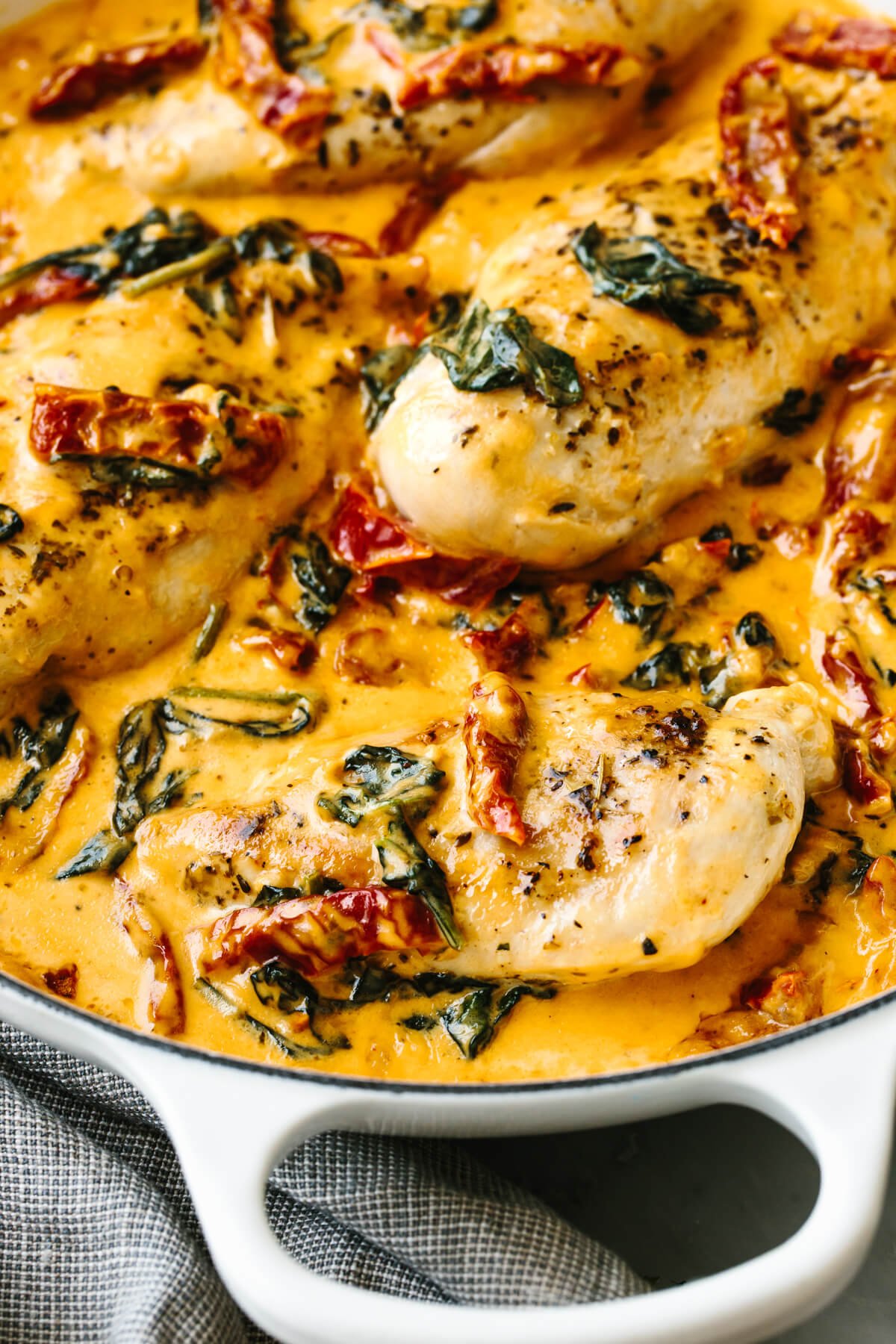 Steal hearts with this creamy tuscan chicken recipe! Seared Italian chicken simmers in a rich and creamy, spinach and sun-dried tomato sauce. A white skillet filled with creamy tuscan chicken