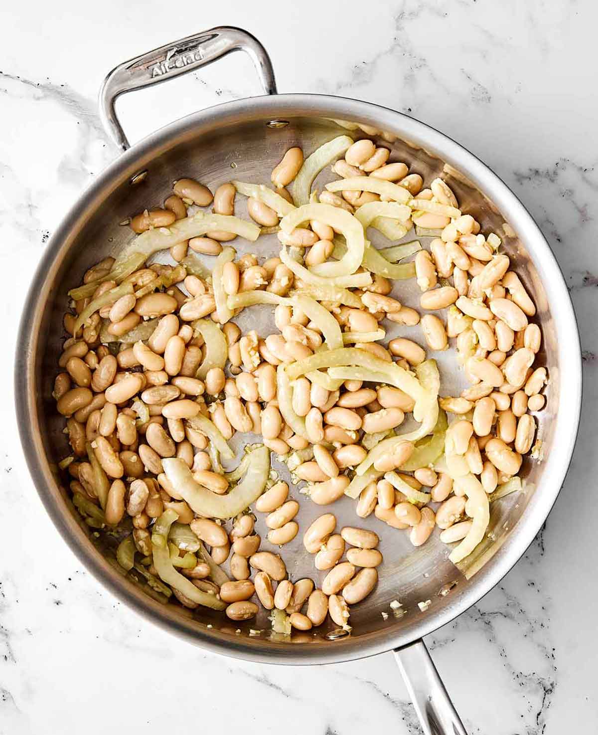 This warm spinach and white bean salad is my nudge to make more warm salads! It’s simple yet savory, healthy, and perfect for colder months. Step two of spinach and white bean salad: add the beans.