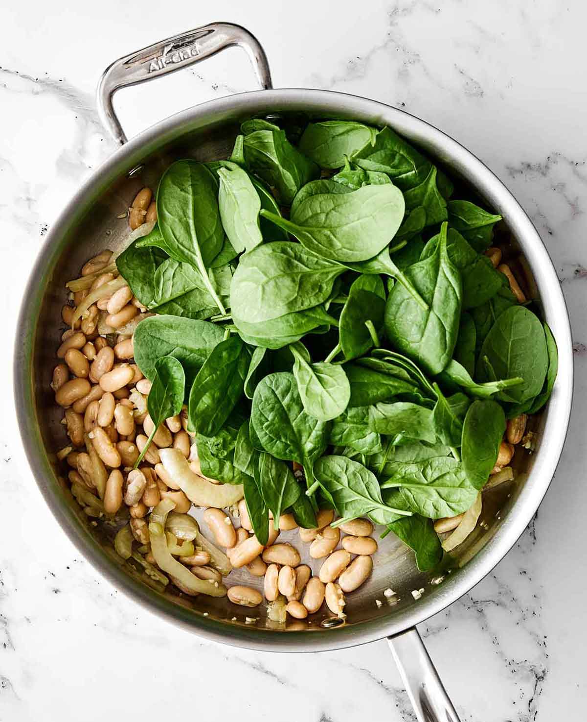 This warm spinach and white bean salad is my nudge to make more warm salads! It’s simple yet savory, healthy, and perfect for colder months. Step three of spinach and white bean salad: add the spinach.